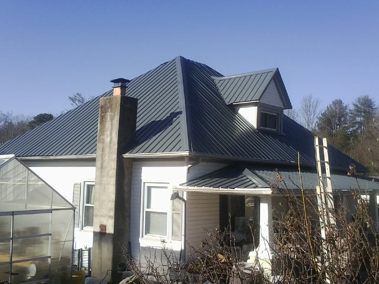 Dark blue standing seam metal roof on a white farmhouse with dormer — Slate & Tile Roof Repair by Roofing Brothers in Pike Road