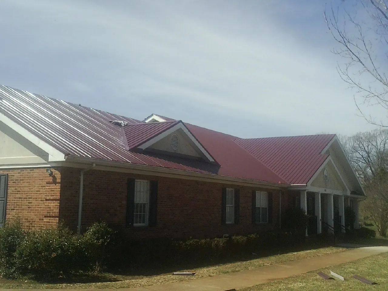 Red metal roof with gabled entries on a long brick building, from a Hail Damage Roof Repair job in Pike Road