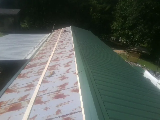 Old rusted panels beside newly installed green metal roofing — Wind Damage Roof Repair by Roofing Brothers in Pike Road