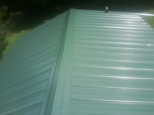 New green metal panels meeting at the ridge of a roof — Flat Roof Repair work by our crew in Pike Road