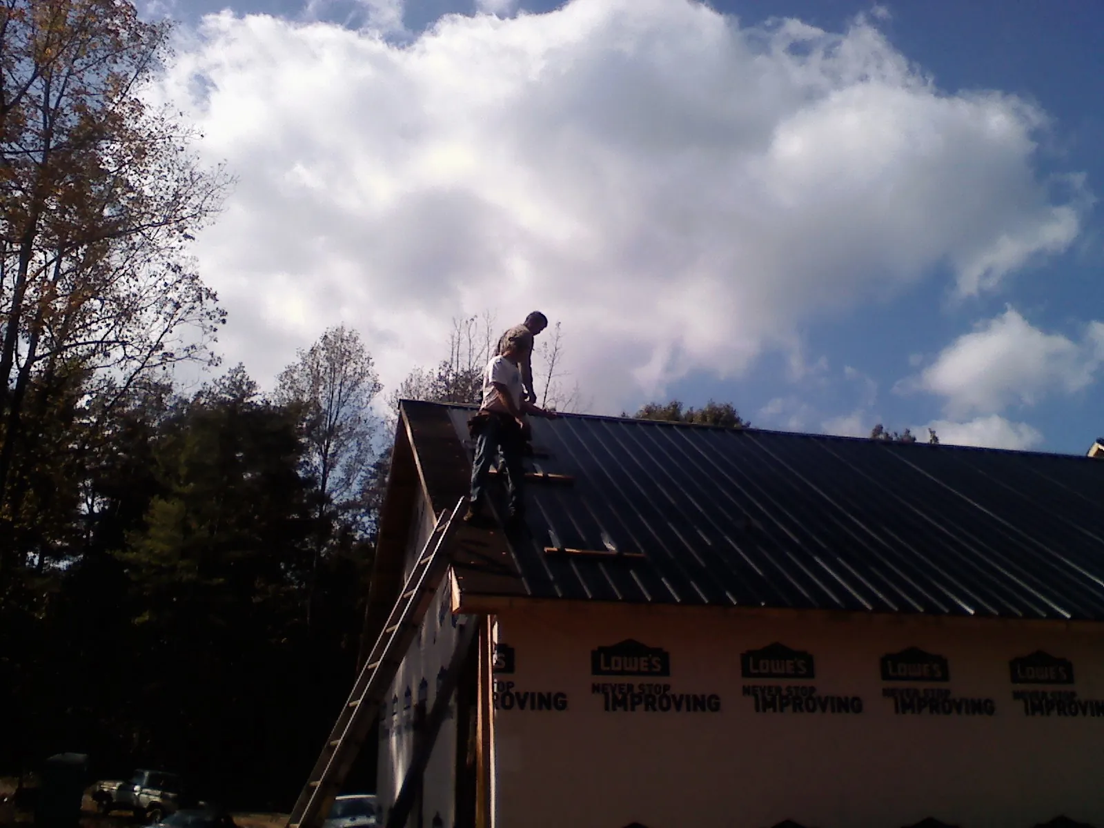 Roofer fastening dark metal panels high against a cloudy sky, from a Roof Inspection job in Pike Road