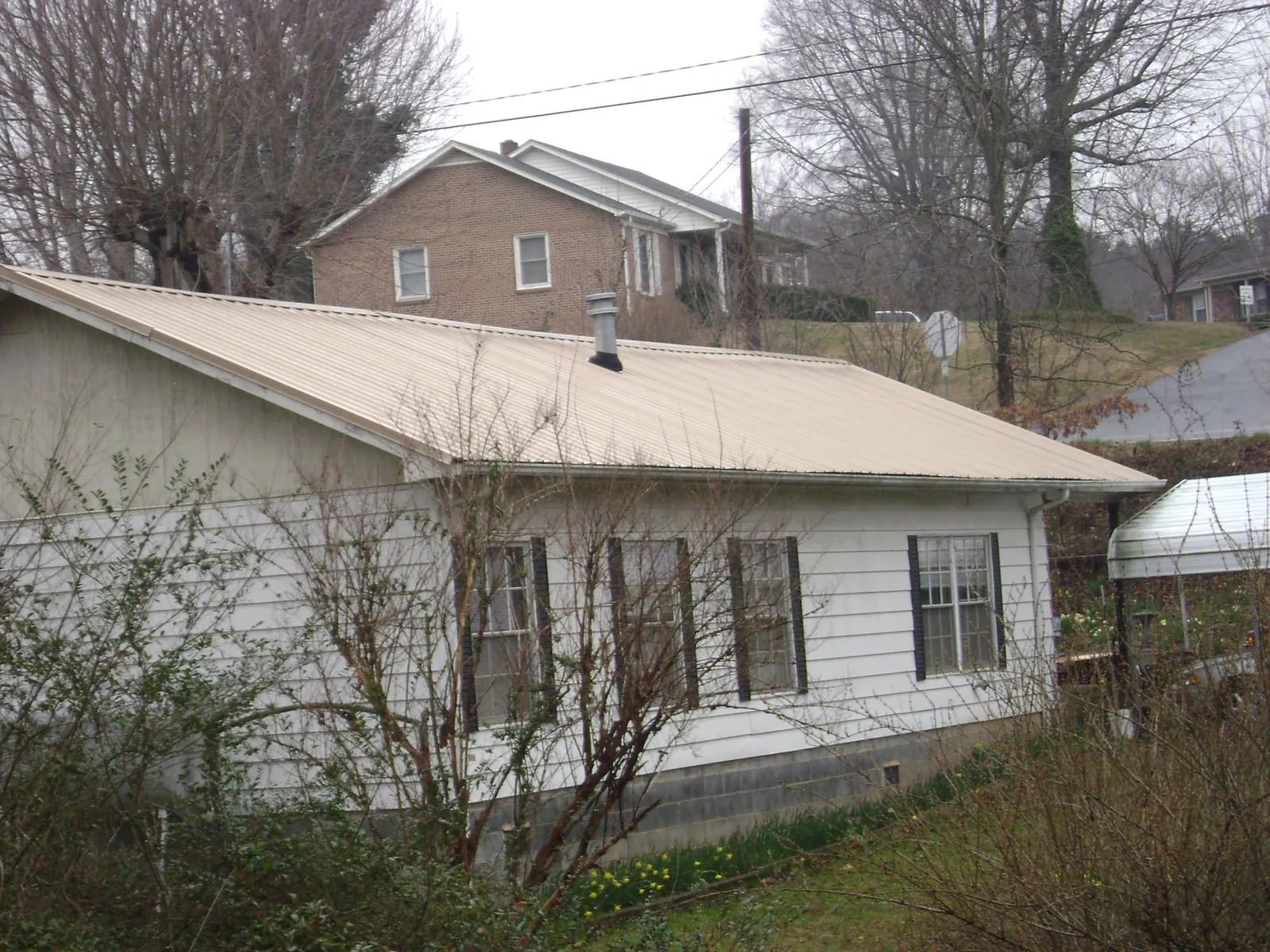 Tan metal roof on a white sided house set into a hillside — Commercial Roofing by Roofing Brothers in Pike Road