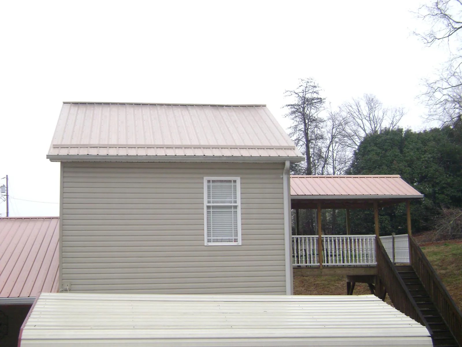 Tan metal roofs on a two story addition and attached porch, from a Roof Replacement job in Pike Road
